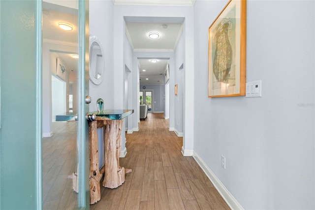 hall featuring baseboards, wood finished floors, and crown molding