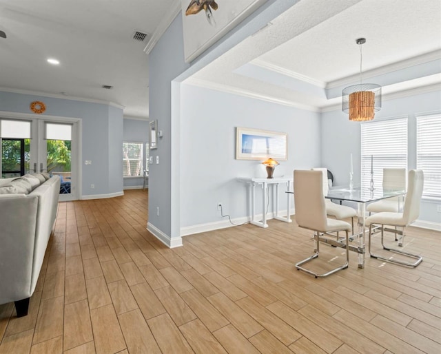 dining space with baseboards, light wood finished floors, a raised ceiling, and crown molding