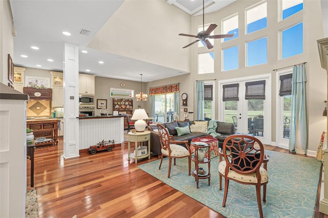 living room featuring sink, french doors, a towering ceiling, ceiling fan with notable chandelier, and light wood-type flooring