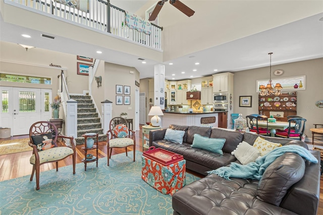 living room with a towering ceiling, wood-type flooring, and ceiling fan with notable chandelier