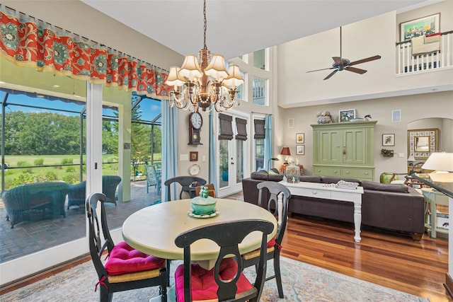 dining room with a high ceiling, ceiling fan with notable chandelier, hardwood / wood-style flooring, and a healthy amount of sunlight