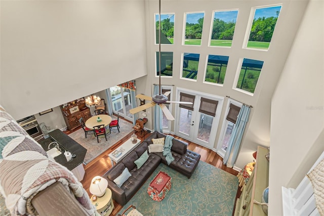 living room featuring ceiling fan with notable chandelier, wood-type flooring, a towering ceiling, and french doors