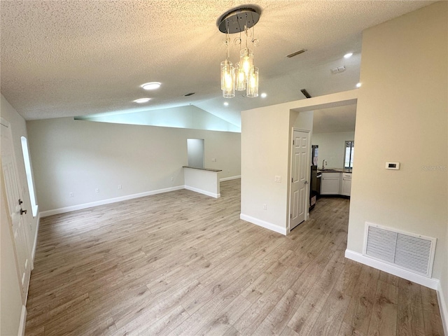 unfurnished room with a textured ceiling, vaulted ceiling, and light wood-type flooring