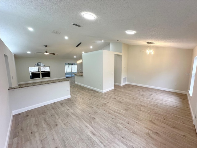 unfurnished living room with ceiling fan with notable chandelier, a textured ceiling, light wood-type flooring, and vaulted ceiling