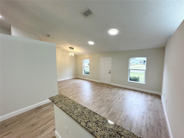 empty room featuring an inviting chandelier, a textured ceiling, and light hardwood / wood-style flooring