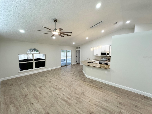 kitchen featuring stainless steel appliances, light stone counters, pendant lighting, vaulted ceiling, and white cabinets