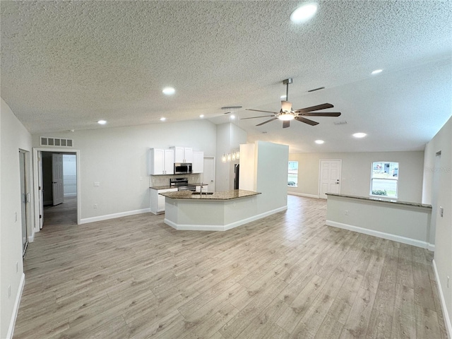 kitchen with white cabinets, light wood-type flooring, a textured ceiling, stone countertops, and stainless steel appliances