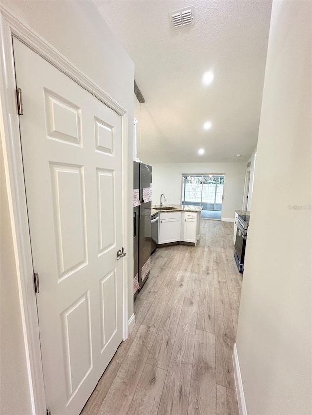 kitchen with white cabinets, light wood-type flooring, sink, and a textured ceiling