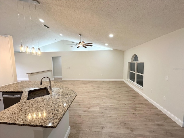 kitchen featuring a textured ceiling, sink, pendant lighting, a center island with sink, and lofted ceiling