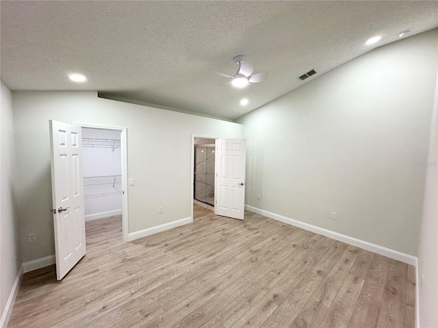 unfurnished bedroom featuring vaulted ceiling, light hardwood / wood-style flooring, ceiling fan, a spacious closet, and a closet