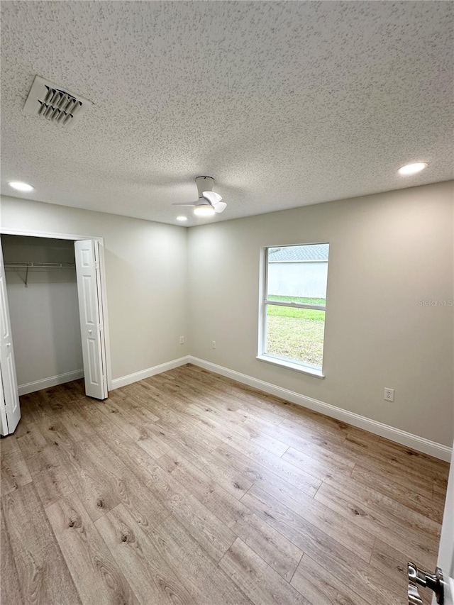 unfurnished bedroom featuring a textured ceiling, light wood-type flooring, a closet, and ceiling fan