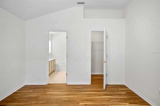 unfurnished bedroom with a walk in closet, connected bathroom, light hardwood / wood-style floors, and a closet