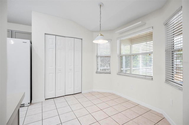 unfurnished bedroom featuring white refrigerator, light tile patterned flooring, lofted ceiling, and a closet