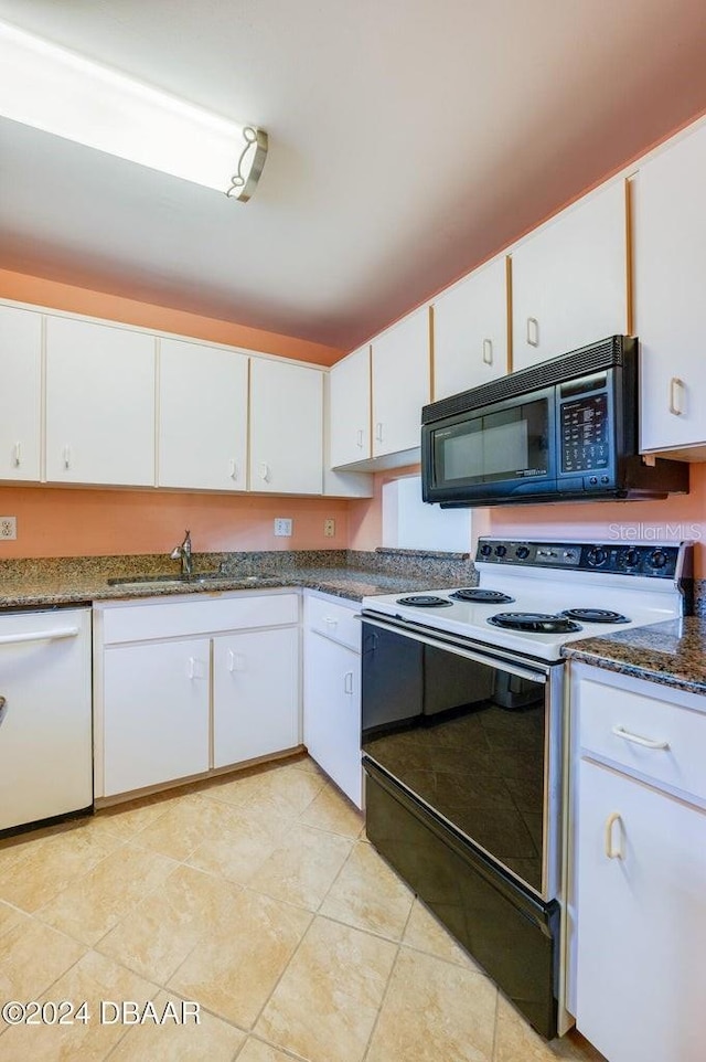 kitchen with light tile patterned floors, white appliances, white cabinetry, and dark stone counters