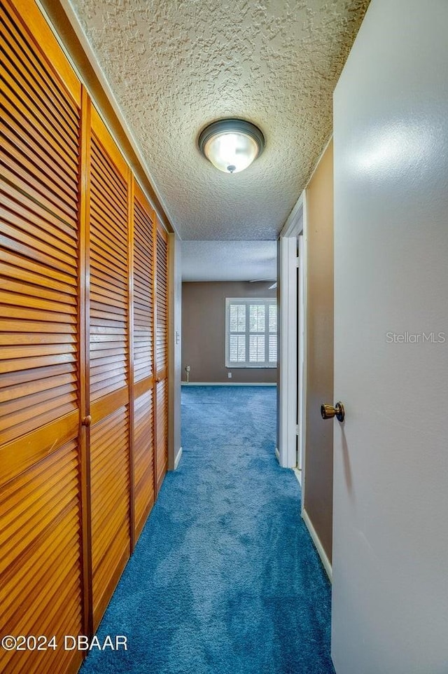 hallway with a textured ceiling and dark carpet