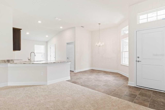 kitchen with sink, light stone counters, decorative light fixtures, dark brown cabinets, and dark carpet