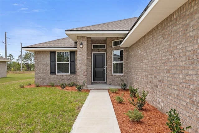 doorway to property featuring roof with shingles, brick siding, and a yard
