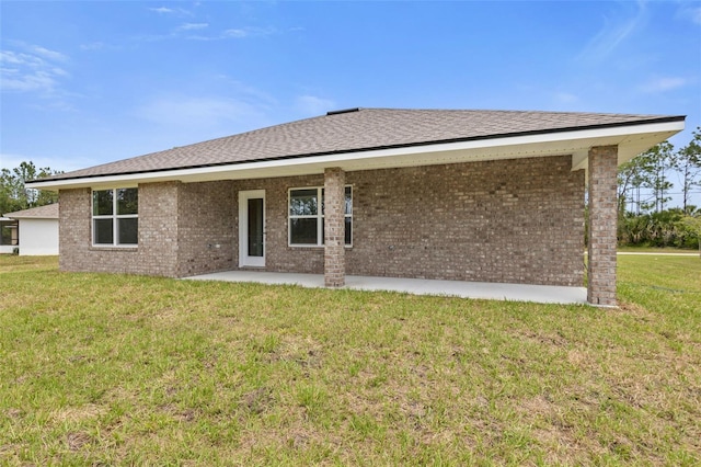 rear view of house with roof with shingles, a yard, a patio area, and brick siding