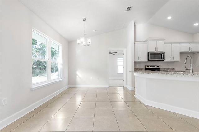 kitchen with appliances with stainless steel finishes, white cabinetry, light stone countertops, light tile patterned flooring, and vaulted ceiling