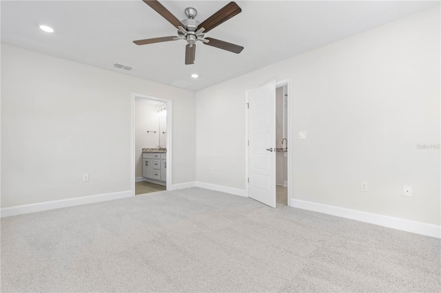 unfurnished bedroom with ceiling fan, ensuite bath, and light carpet