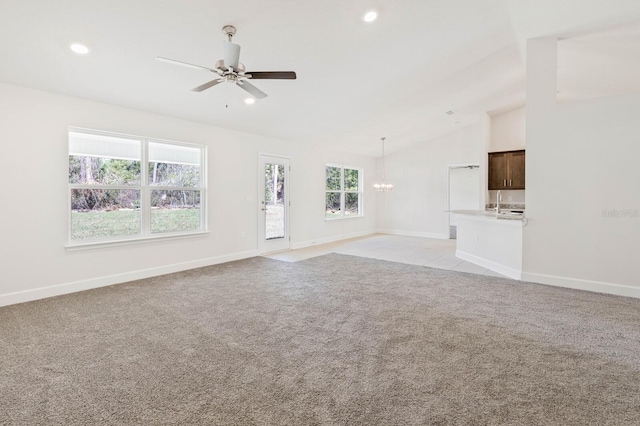 unfurnished living room featuring lofted ceiling, ceiling fan with notable chandelier, light colored carpet, and a healthy amount of sunlight