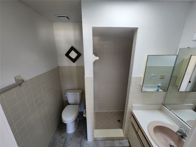 bathroom with vanity, tile patterned floors, toilet, tile walls, and a tile shower