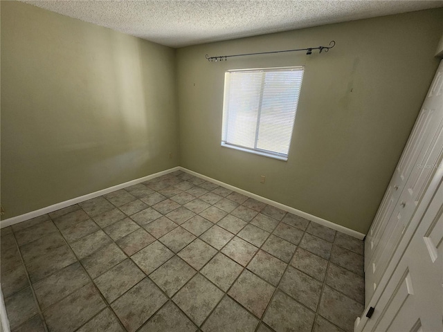 tiled empty room with a textured ceiling and baseboards