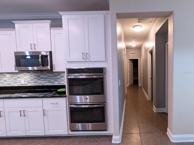 kitchen featuring dark stone counters, white cabinets, decorative backsplash, dark tile patterned floors, and stainless steel appliances