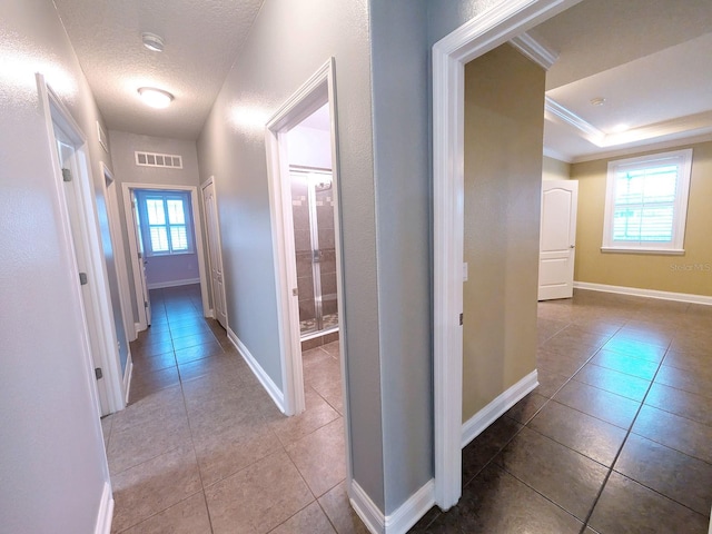 hallway featuring a raised ceiling, a wealth of natural light, crown molding, and light tile patterned floors