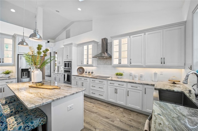 kitchen with appliances with stainless steel finishes, wall chimney exhaust hood, white cabinetry, backsplash, and hanging light fixtures