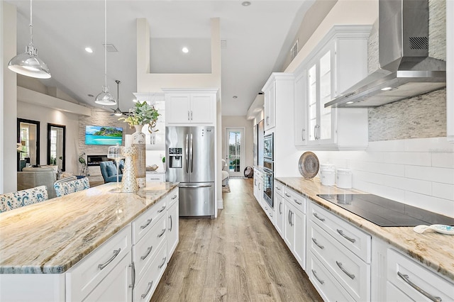 kitchen featuring decorative light fixtures, white cabinetry, wall chimney range hood, stainless steel appliances, and a large fireplace