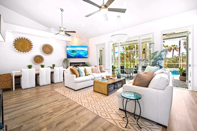 living room featuring lofted ceiling, a fireplace, ceiling fan with notable chandelier, and light hardwood / wood-style flooring