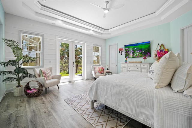 bedroom featuring ceiling fan, access to exterior, a tray ceiling, light hardwood / wood-style flooring, and french doors