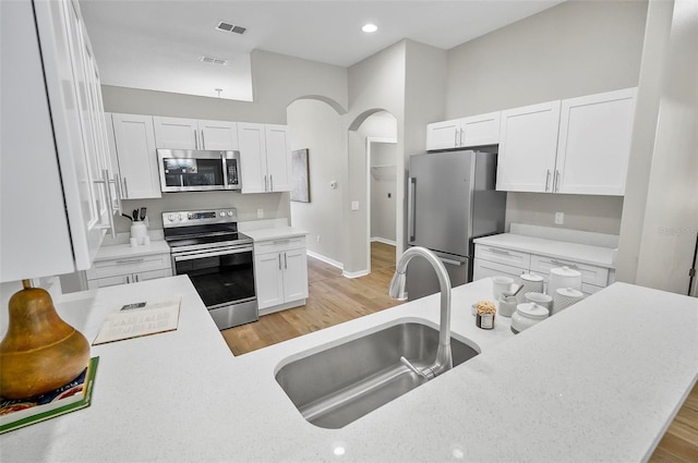 kitchen with light stone countertops, appliances with stainless steel finishes, sink, light hardwood / wood-style flooring, and white cabinetry