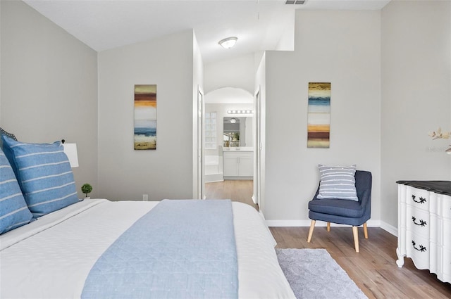 bedroom featuring ensuite bath, lofted ceiling, and light wood-type flooring