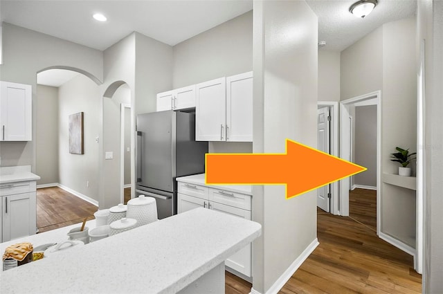 kitchen featuring a towering ceiling, white cabinetry, light hardwood / wood-style floors, a kitchen island, and stainless steel refrigerator