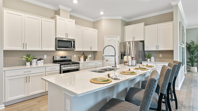 kitchen with white cabinetry, ornamental molding, a kitchen island with sink, and appliances with stainless steel finishes