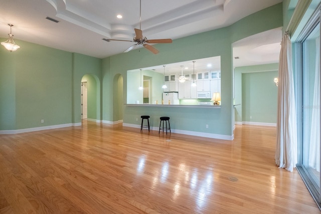 unfurnished living room with a tray ceiling, ceiling fan, and light hardwood / wood-style floors