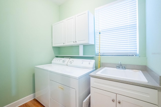 clothes washing area featuring light hardwood / wood-style floors, cabinets, sink, and washing machine and clothes dryer