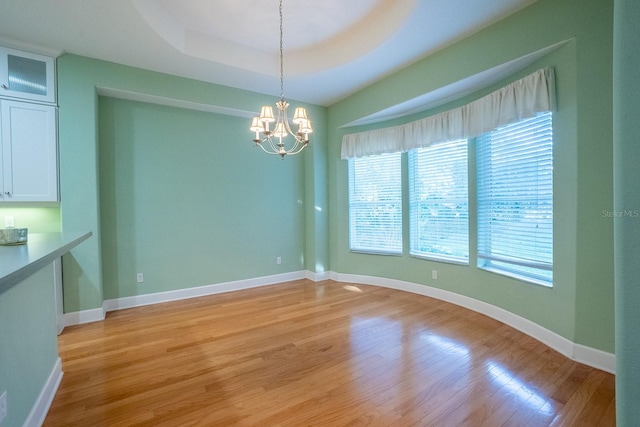 unfurnished dining area featuring a chandelier, light hardwood / wood-style floors, and a raised ceiling