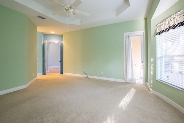 spare room with a raised ceiling, ceiling fan, plenty of natural light, and light colored carpet