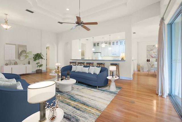 living room with ceiling fan, light hardwood / wood-style floors, and a raised ceiling