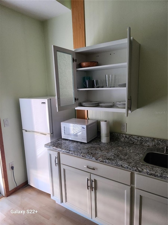 kitchen with white cabinetry, sink, dark stone counters, white appliances, and light wood-type flooring