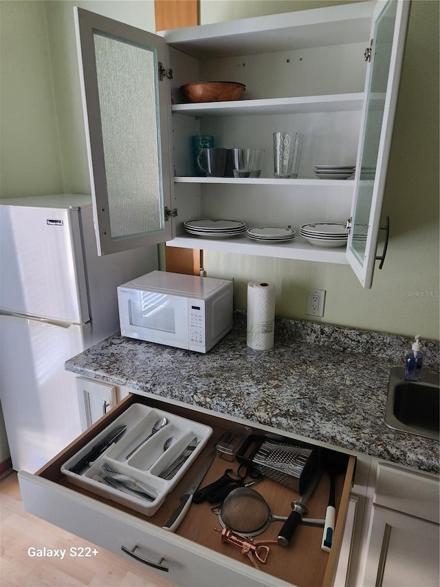 kitchen featuring sink, dark stone counters, white appliances, and light wood-type flooring