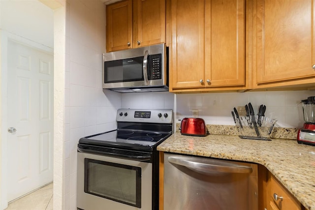 kitchen with decorative backsplash, light stone counters, light tile patterned floors, and stainless steel appliances