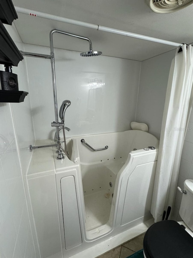 bathroom featuring toilet, a tub to relax in, and tile patterned floors