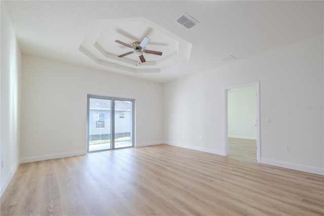 spare room featuring a raised ceiling, ceiling fan, and light wood-type flooring