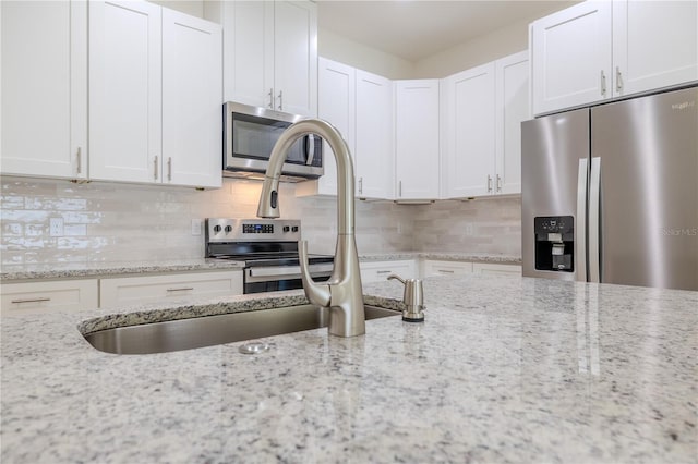 kitchen featuring light stone counters, white cabinetry, backsplash, and appliances with stainless steel finishes