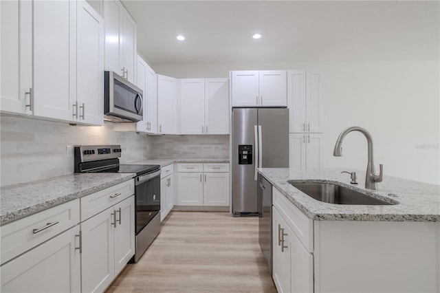 kitchen with light stone countertops, sink, stainless steel appliances, a center island with sink, and white cabinets