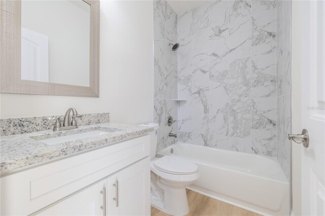 full bathroom with hardwood / wood-style floors, vanity, tiled shower / bath combo, and toilet